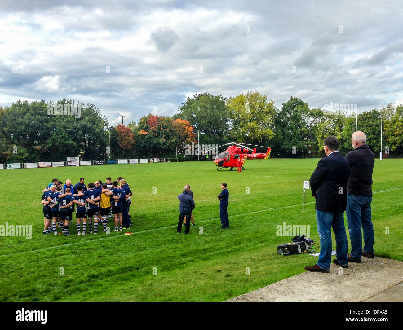 Woodford Green, London, UK. 30th September 2017. Officials look on as London’s  Air Ambulance helicopter G-LNDN lands at Woodford Rugby Football Club's Highams ground in Woodford Green in response to a report of a spectator suffering a heart attack. The Woodford v Chelmsford match was suspended for 40 minutes whilst paramedics attended to the casualty who was able to leave by road.  Woodford went on to win the match. The Air Ambulance is supported by London Freemasons.  Credit: Mark Dunn/ Alamy Live News Stock Photo