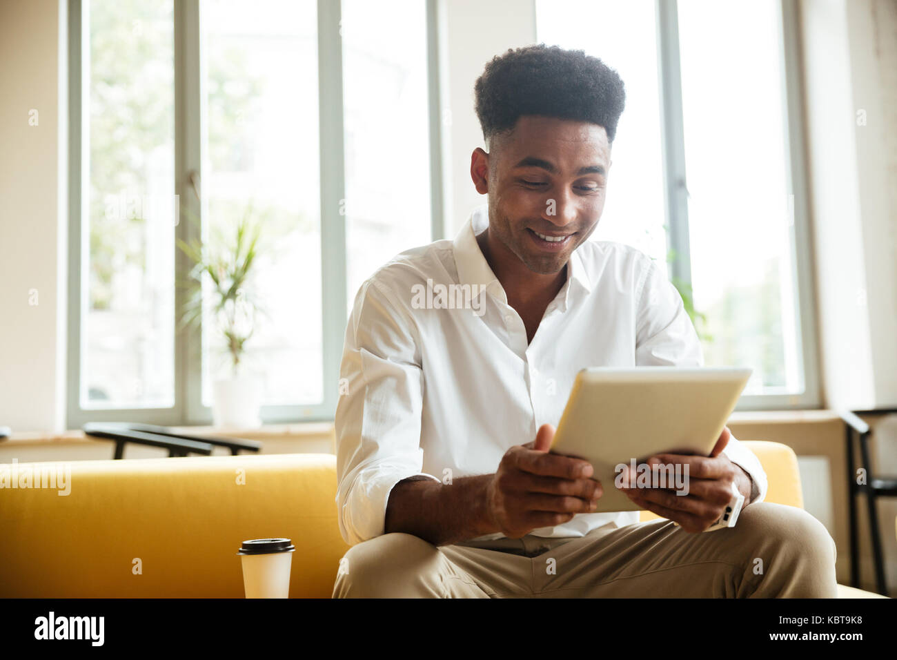Image of cheerful young african man sitting coworking by tablet ...