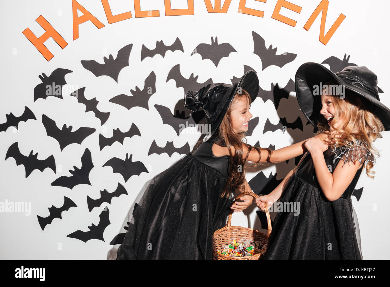 Couple of two little girls dressed in halloween costumes fighting for the  basket full with candy with bats on a background Stock Photo - Alamy