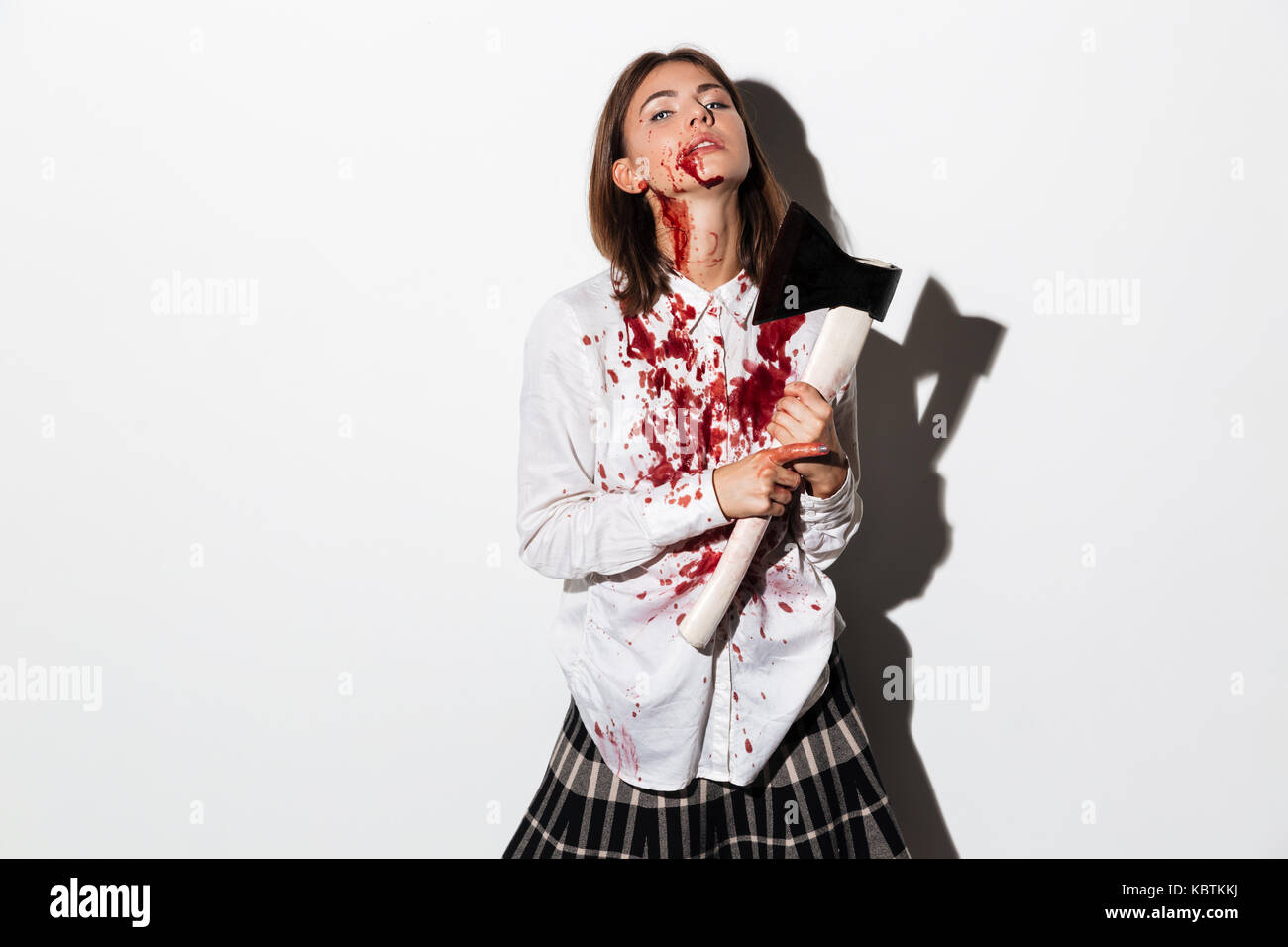 Mad zombie woman bleading while holding an axe at her throat isolated over white background Stock Photo