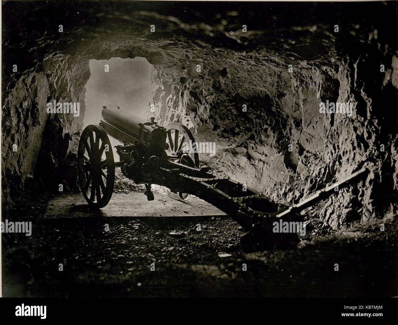 This historical image depicts a mountain howitzer stationed in a cave ...