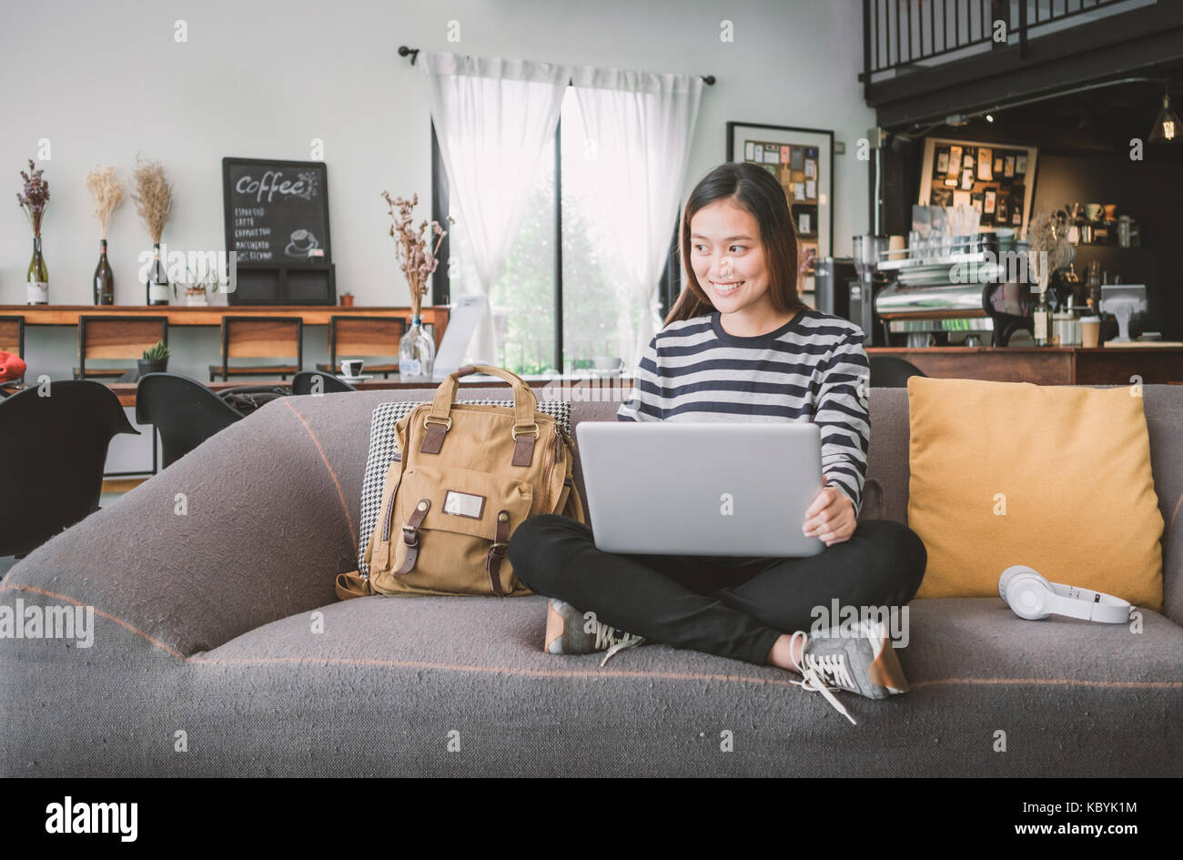 Asian teenager girl using laptop computer and listening music on sofa ...