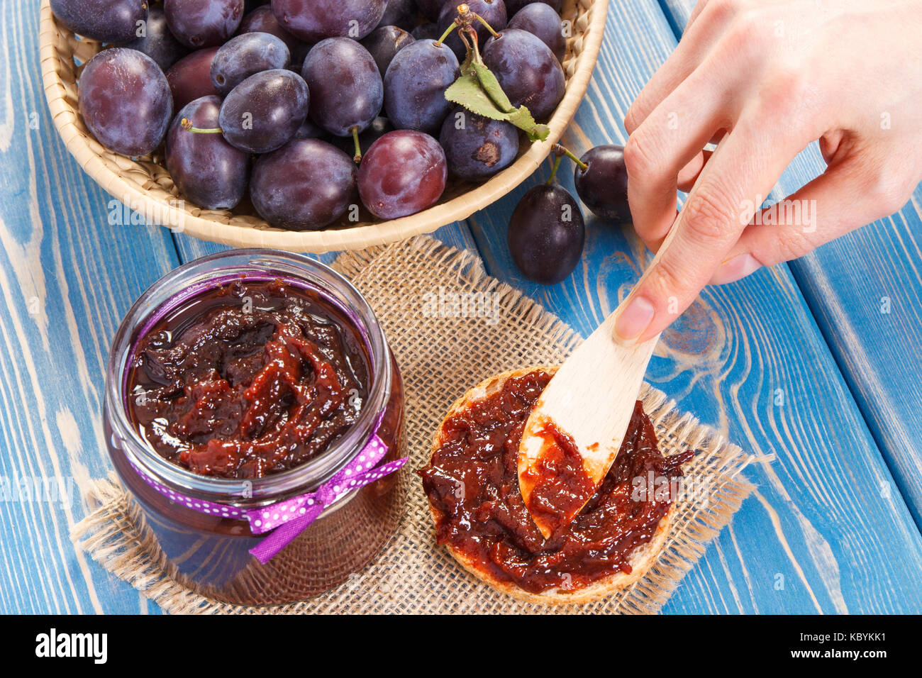 Hand of woman with wooden knife preparing sandwiches with plum marmalade or jam, concept of healthy sweet snack or dessert Stock Photo