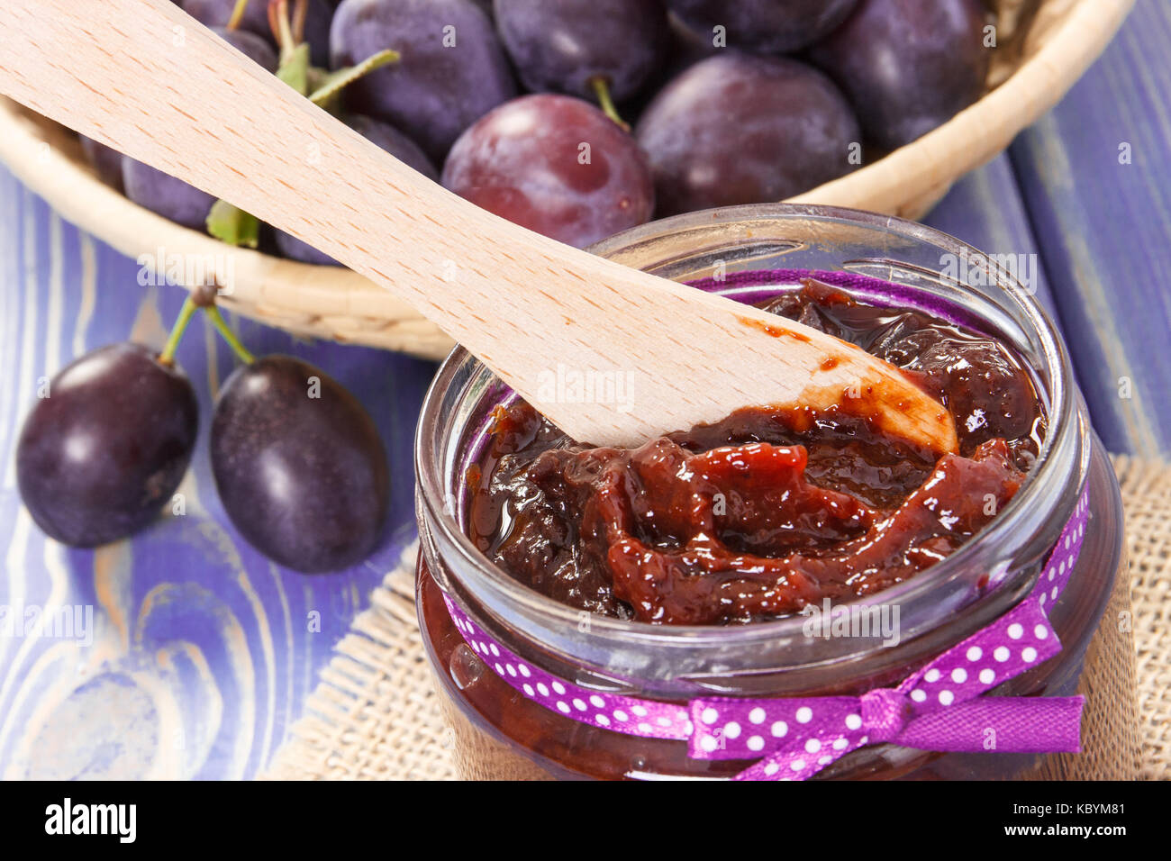 Wooden knife and homemade plum marmalade or jam in glass jar, concept of healthy sweet snack, dessert or breakfast Stock Photo