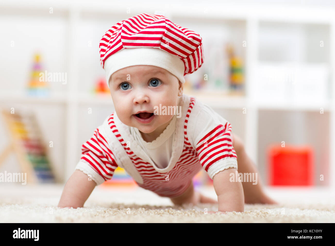 Six months old baby girl crawling on fluffy floor in nursery Stock Photo