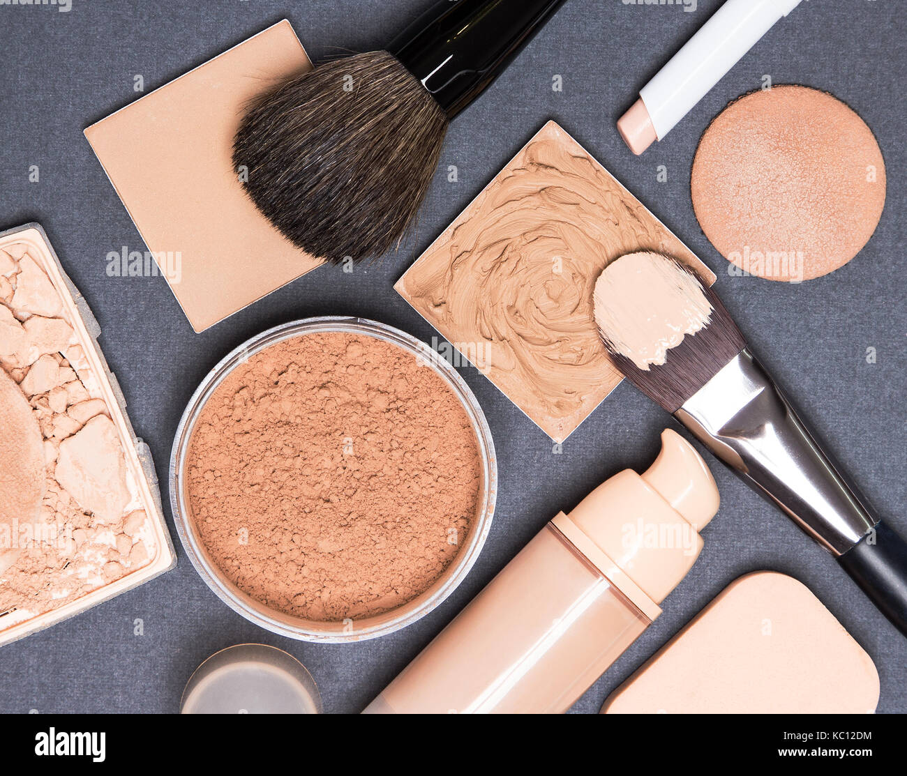 Close-up of concealer pencil, corrector, open liquid foundation bottle and jar of loose powder, crushed compact powder, makeup brushes and sponges Stock Photo