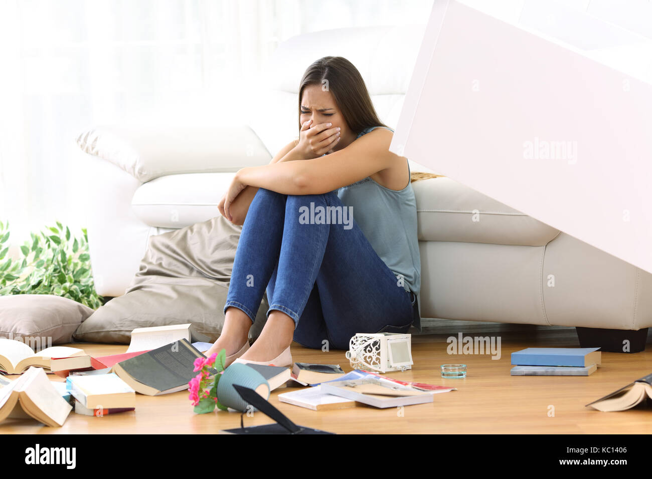 Sad homeowner lamenting after robbery sitting on the floor of the living room at home Stock Photo