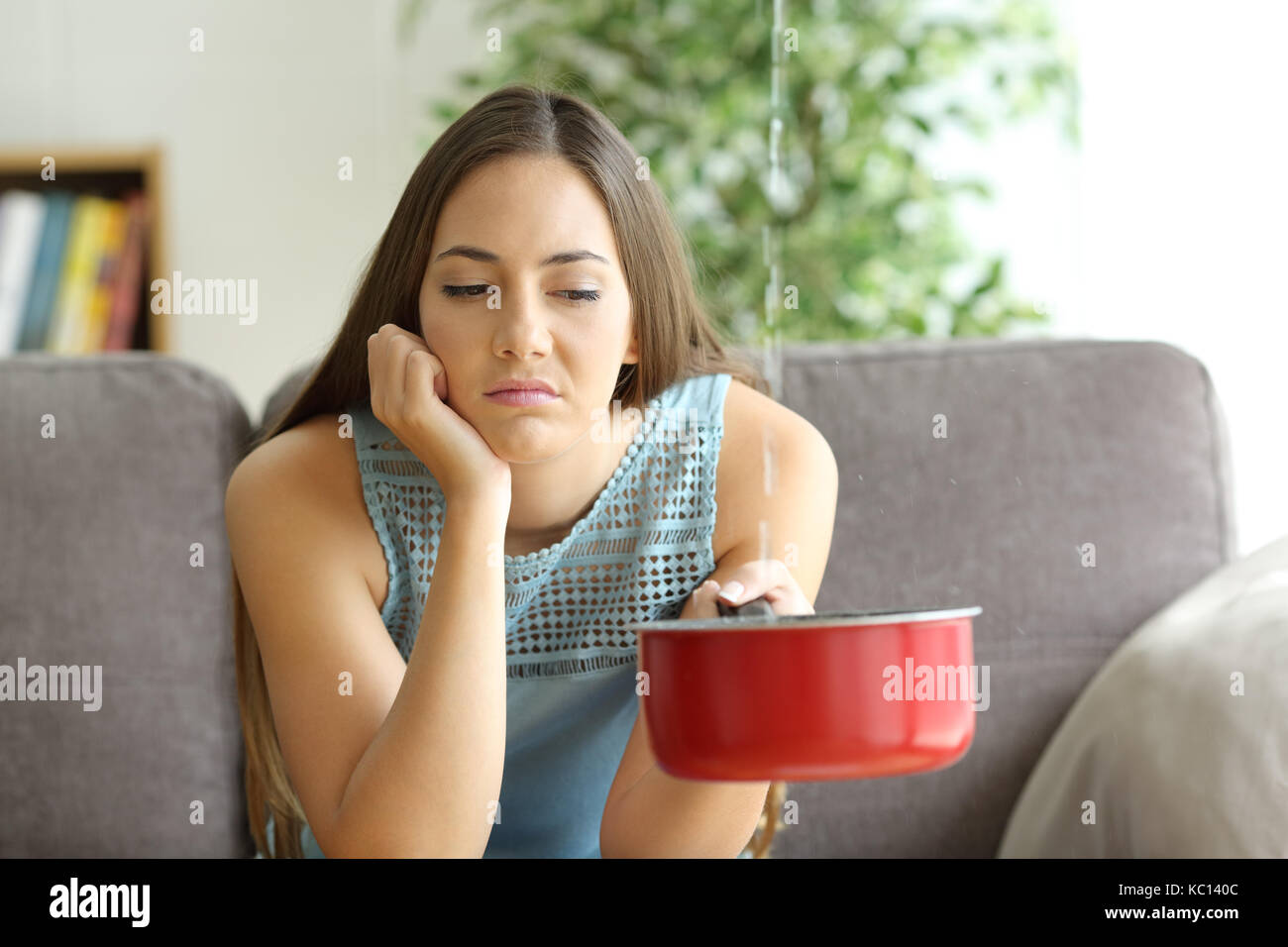 Frustrated homeowner watching ceiling leaks sitting on a couch at home Stock Photo