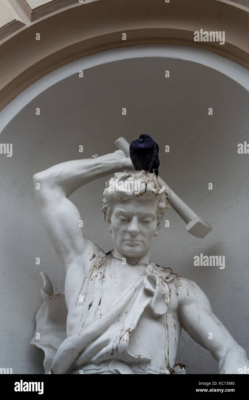 Blacksmith statue with pigeon on head. Stock Photo
