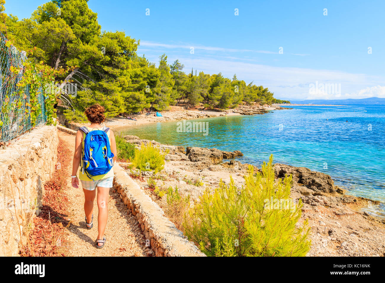Young woman tourist with backpack walking on coastal path along sea near Bol town, Brac island, Croatia Stock Photo
