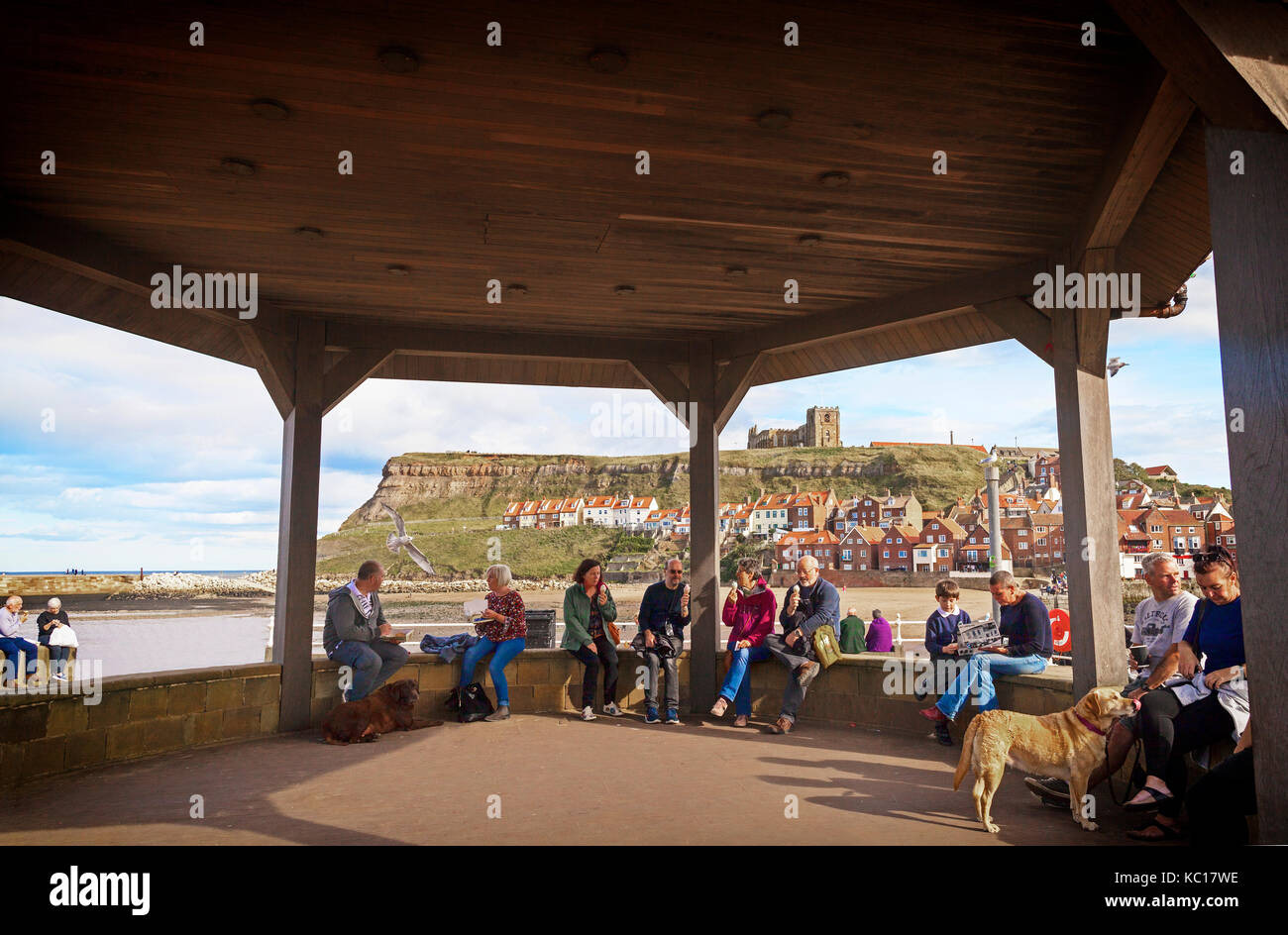 Eating fish and chips and/or icecream  in the bandstand at Scotch Head beside the harbour, with Whitby Abbey Behind, North Yorkshire Coast, England Stock Photo