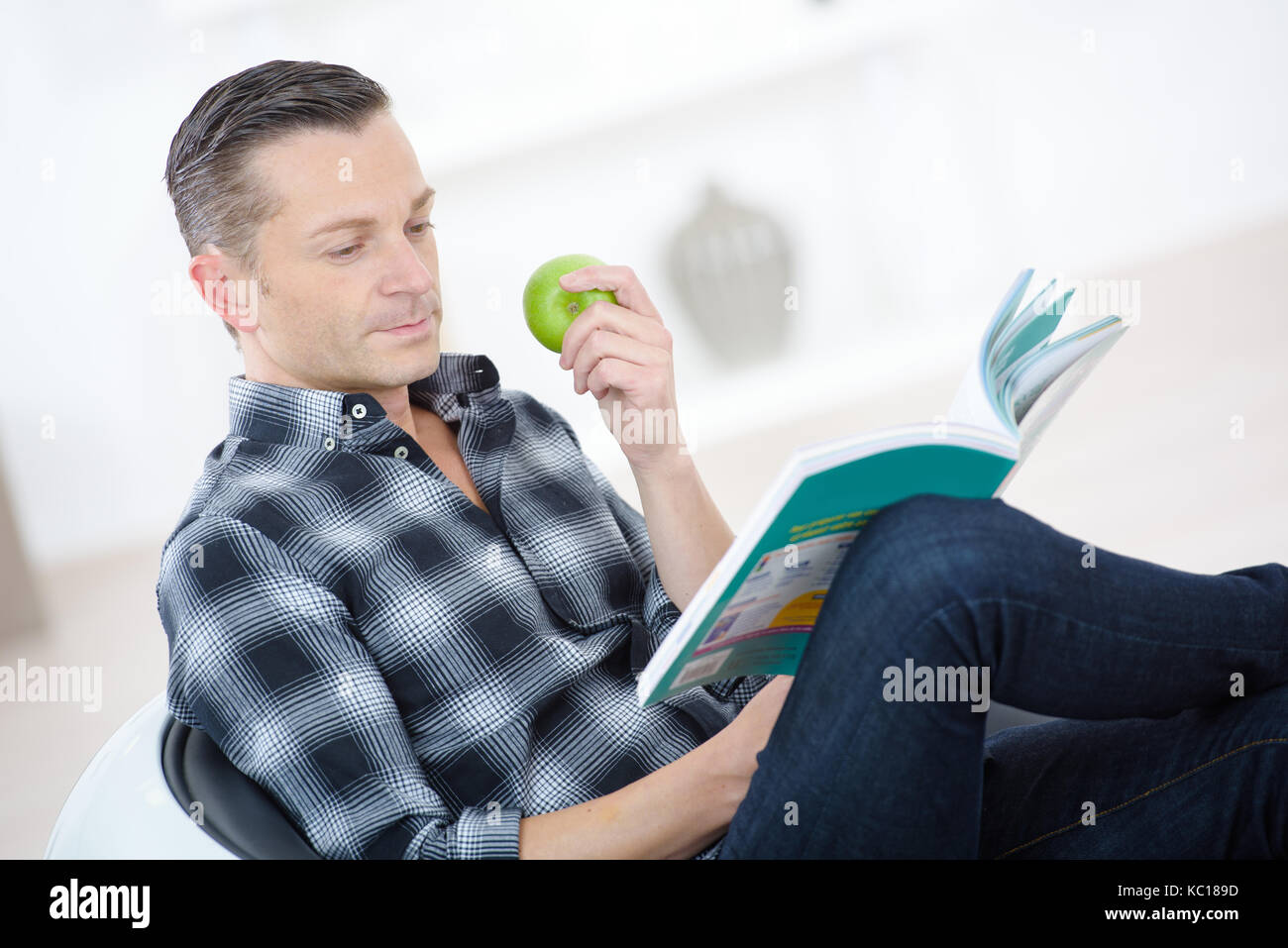 man eating apple and reading while laying on the couch Stock Photo - Alamy