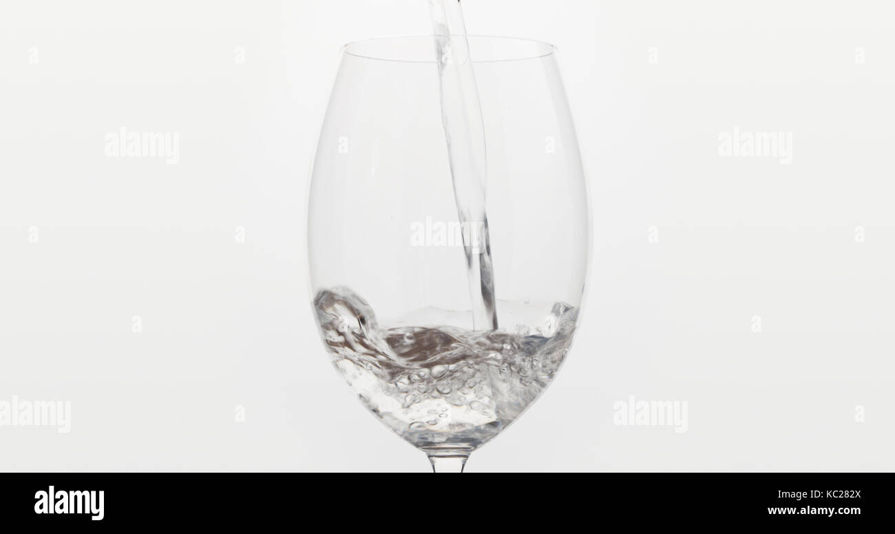 pouring water into wine glass over white background, wide photo Stock