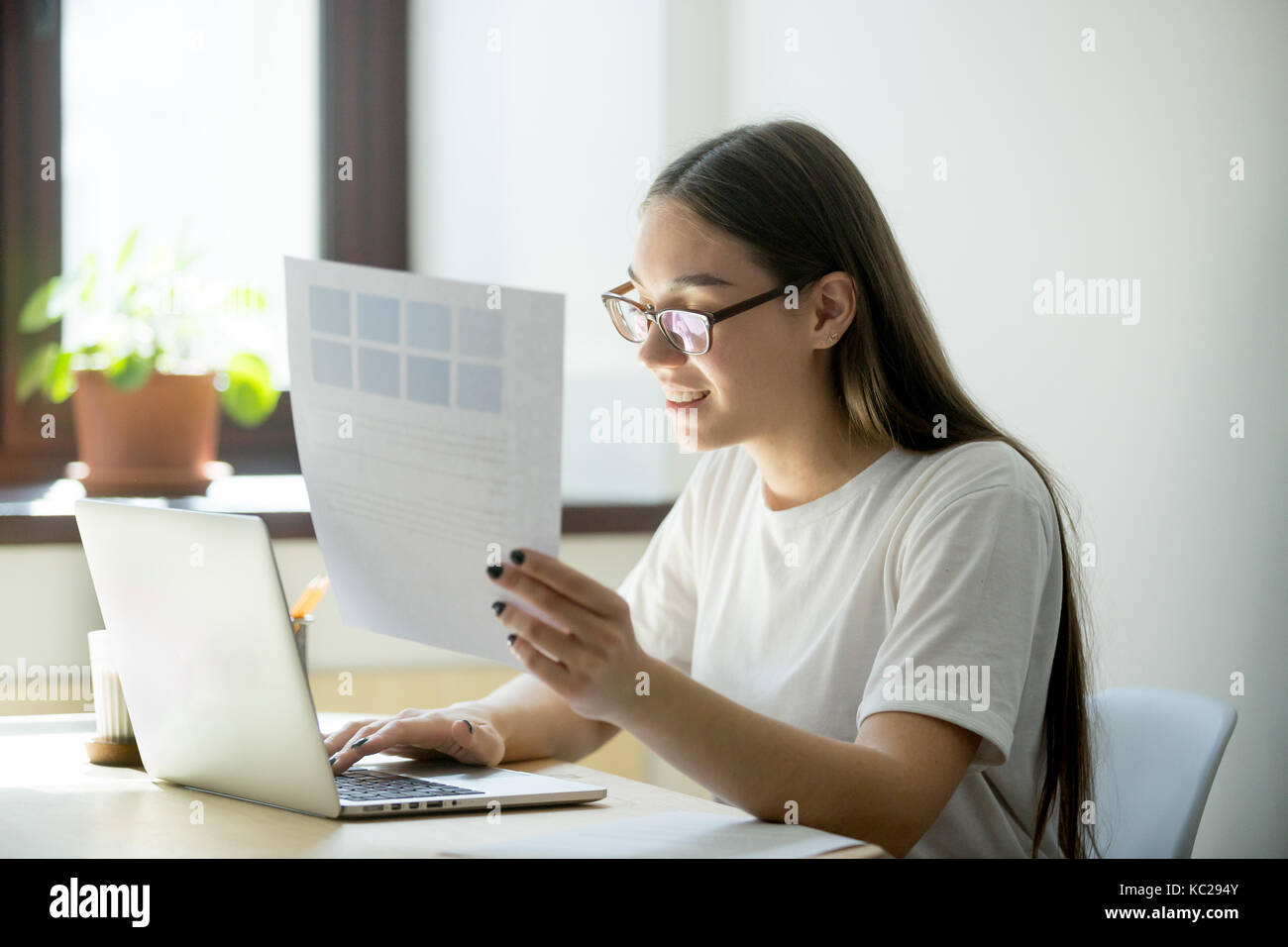 Young happy designer woman working on laptop holding pantone color swatch palette for house interior renovation project. Attractive model choosing col Stock Photo