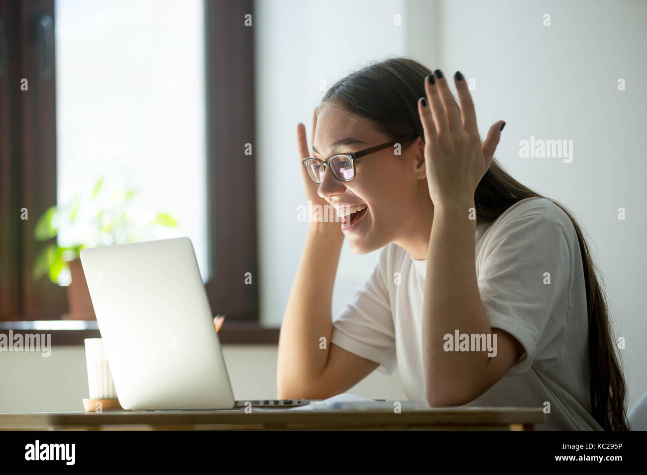 Young adult woman receiving good news via her laptop computer, reading email, videochatting with friends or watching a movie on online tv. Stock Photo