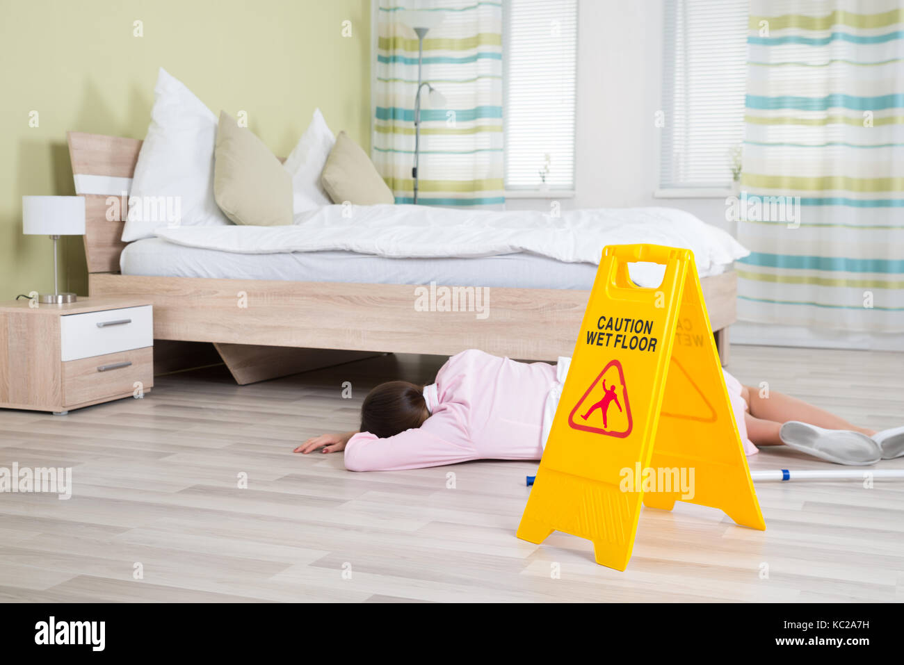 Young Female Housekeeper Unconscious Near Wet Floor Sign In Hotel Room Stock Photo