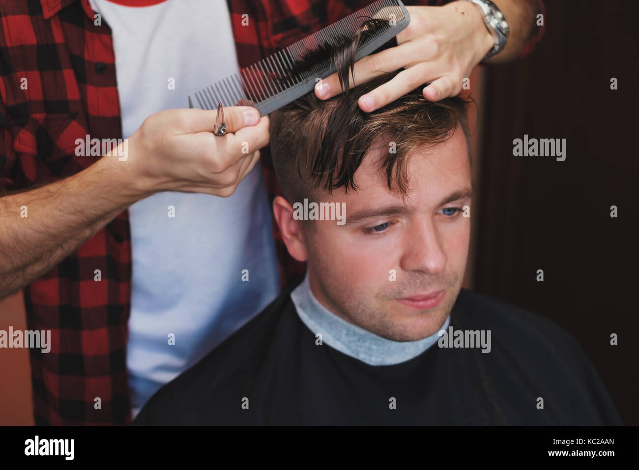 Caucasian young man in Barber is cuttinhg his hair in