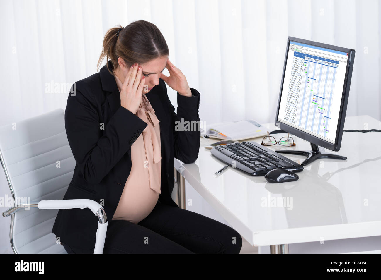 Pregnant Businesswoman Having Headache Sitting In A Chair At Desk Stock