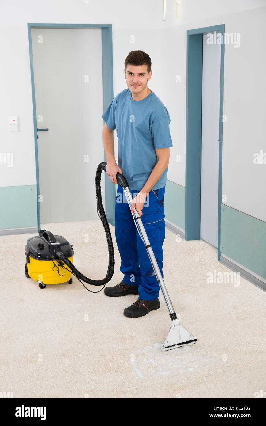 Young Male Cleaner In Uniform Vacuuming Floor Stock Photo