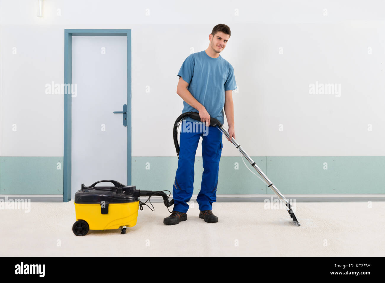 Young Male Cleaner In Uniform Vacuuming Floor Stock Photo