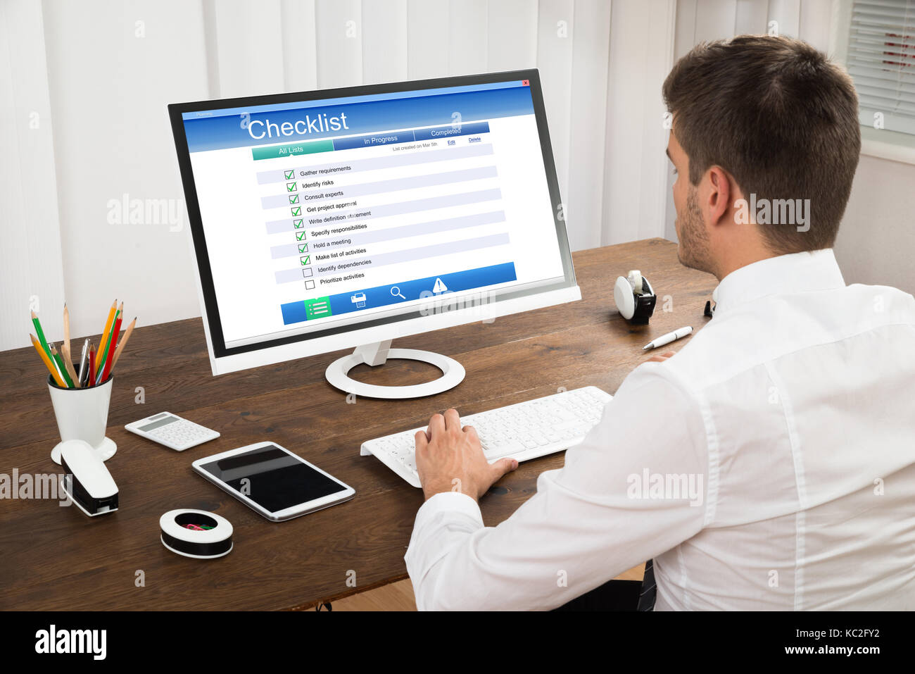 Young Businessman Filling Checklist Form On Computer At Wooden Desk Stock Photo