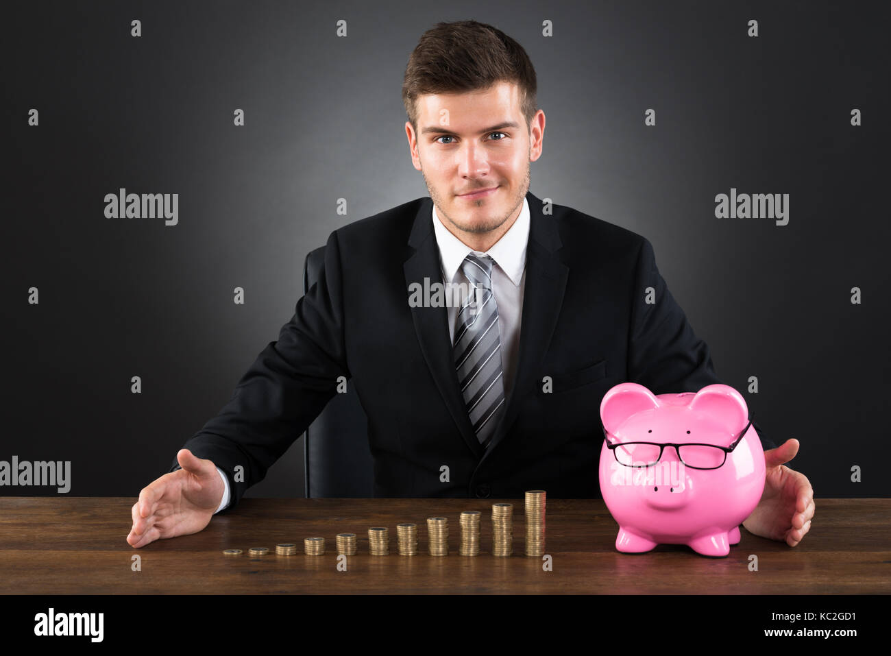 Young Businessman Protecting Stack Of Coins And Piggybank At Desk Stock Photo