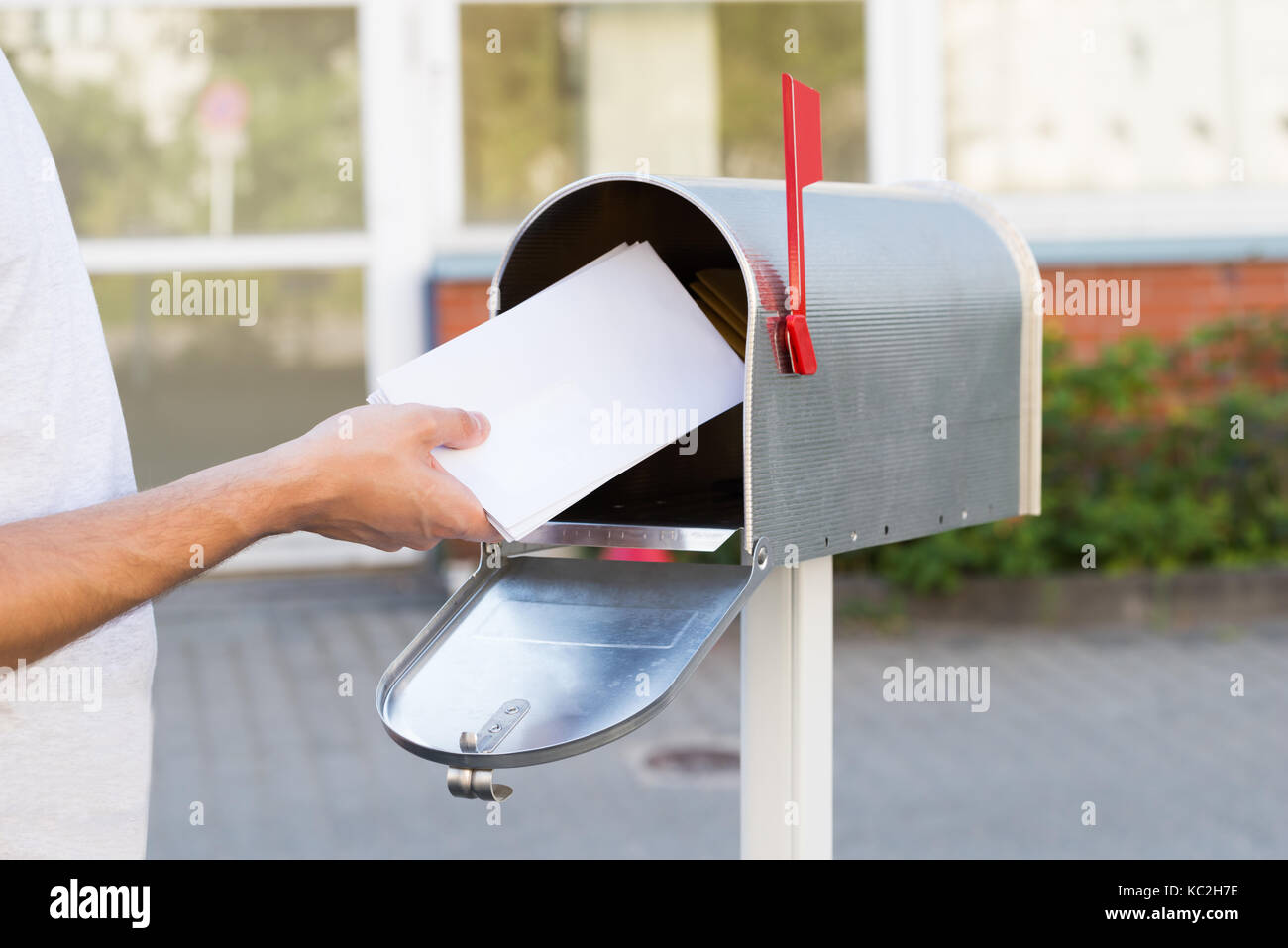Close-up Of Person Putting Stack Of Letters In Mailbox Stock Photo