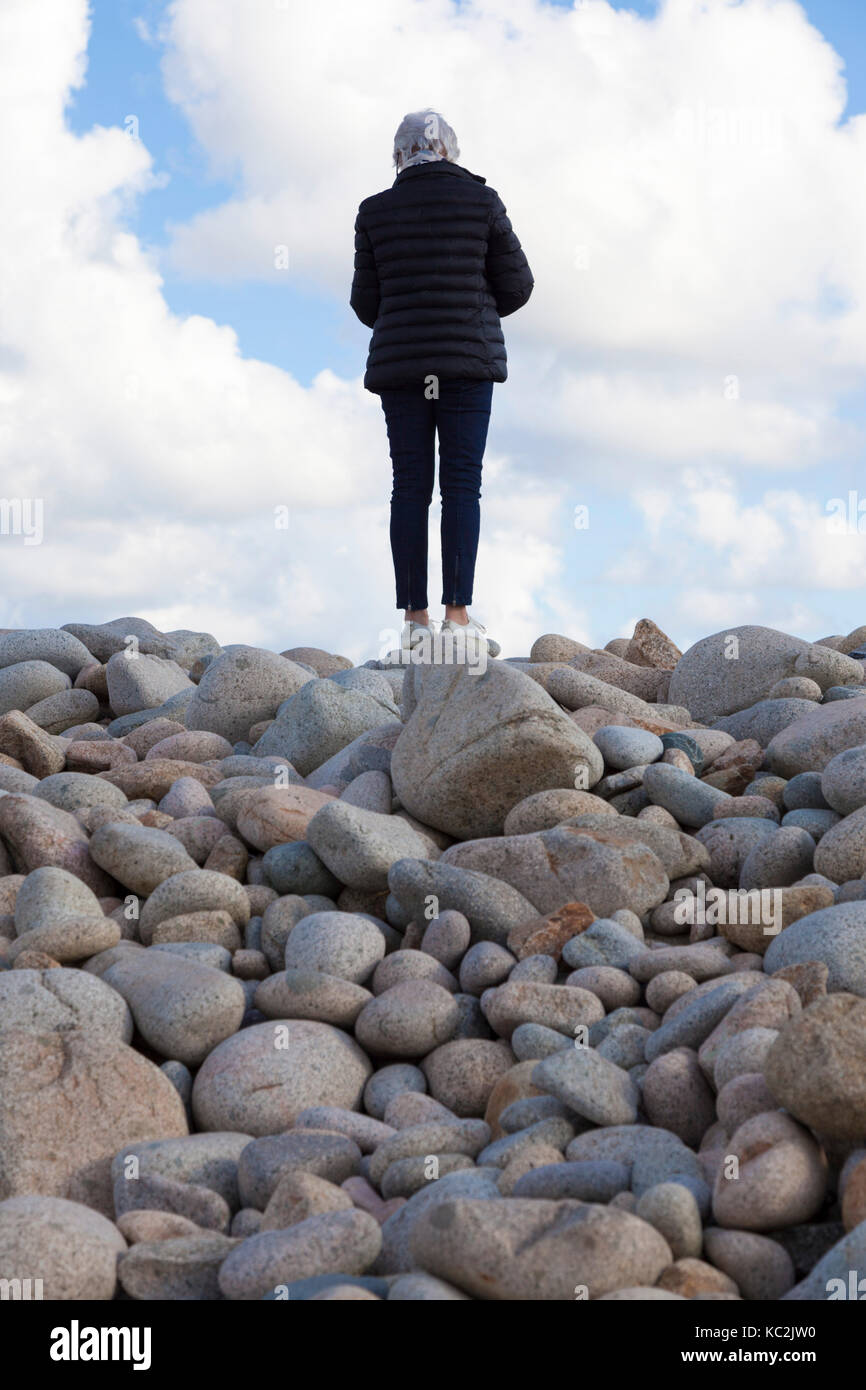 On the North West coast of the Brehat island (Brittany - France),a senior citizen tourist looking for a perfect pebble as a souvenir. Stock Photo