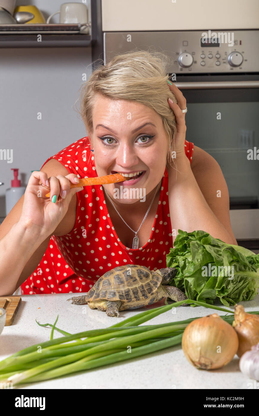 Tortoise eating roman salad while young woman bites carrot Stock Photo