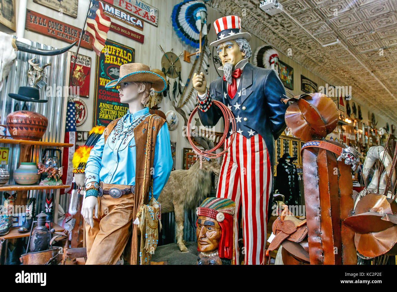 Colorful wooden statues of Uncle Sam and a cowgirl dressed in blue shirt stand among a variety of other items in a Wild West store. Stock Photo