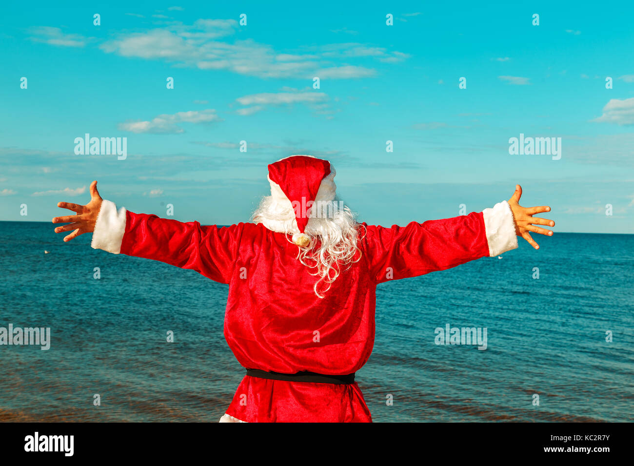 Santa Claus is standing on the beach with arms outstretched. View from ...