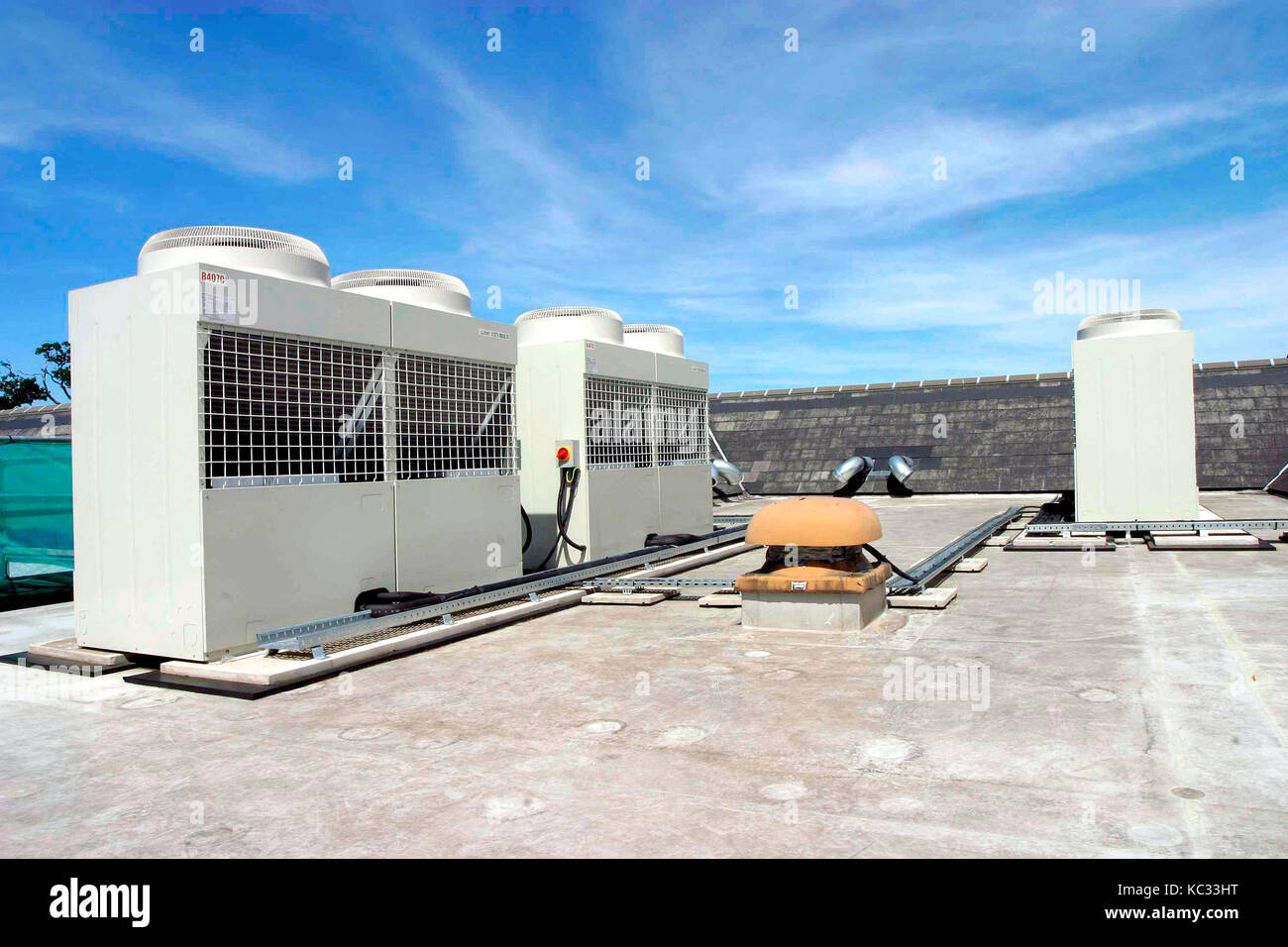 Air conditioning units on the roof of a tall building, with a blue sky behind. Stock Photo