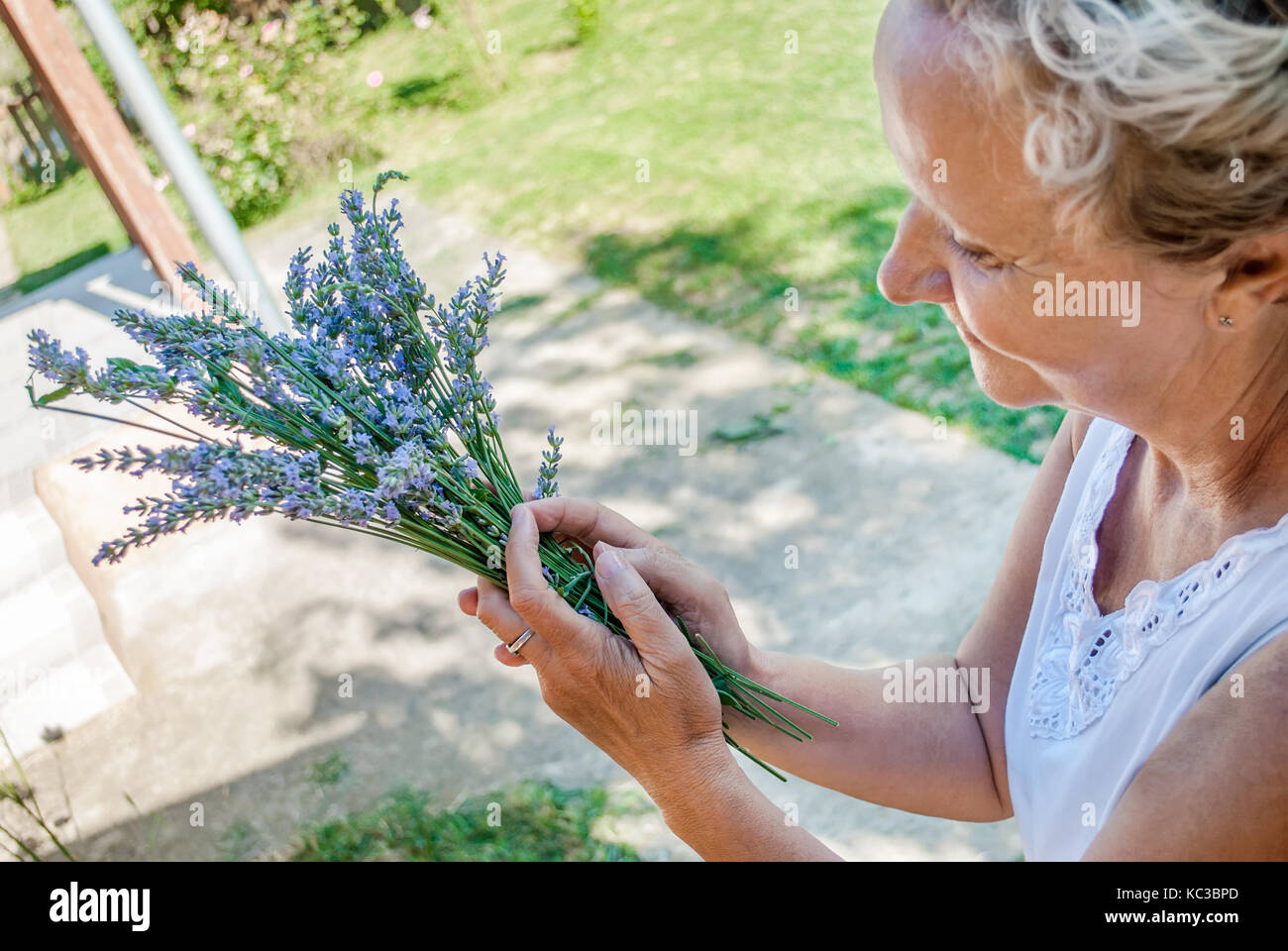 Beautiful middle-aged woman, in her yard in the countryside, arranges flowers of lavender Stock Photo