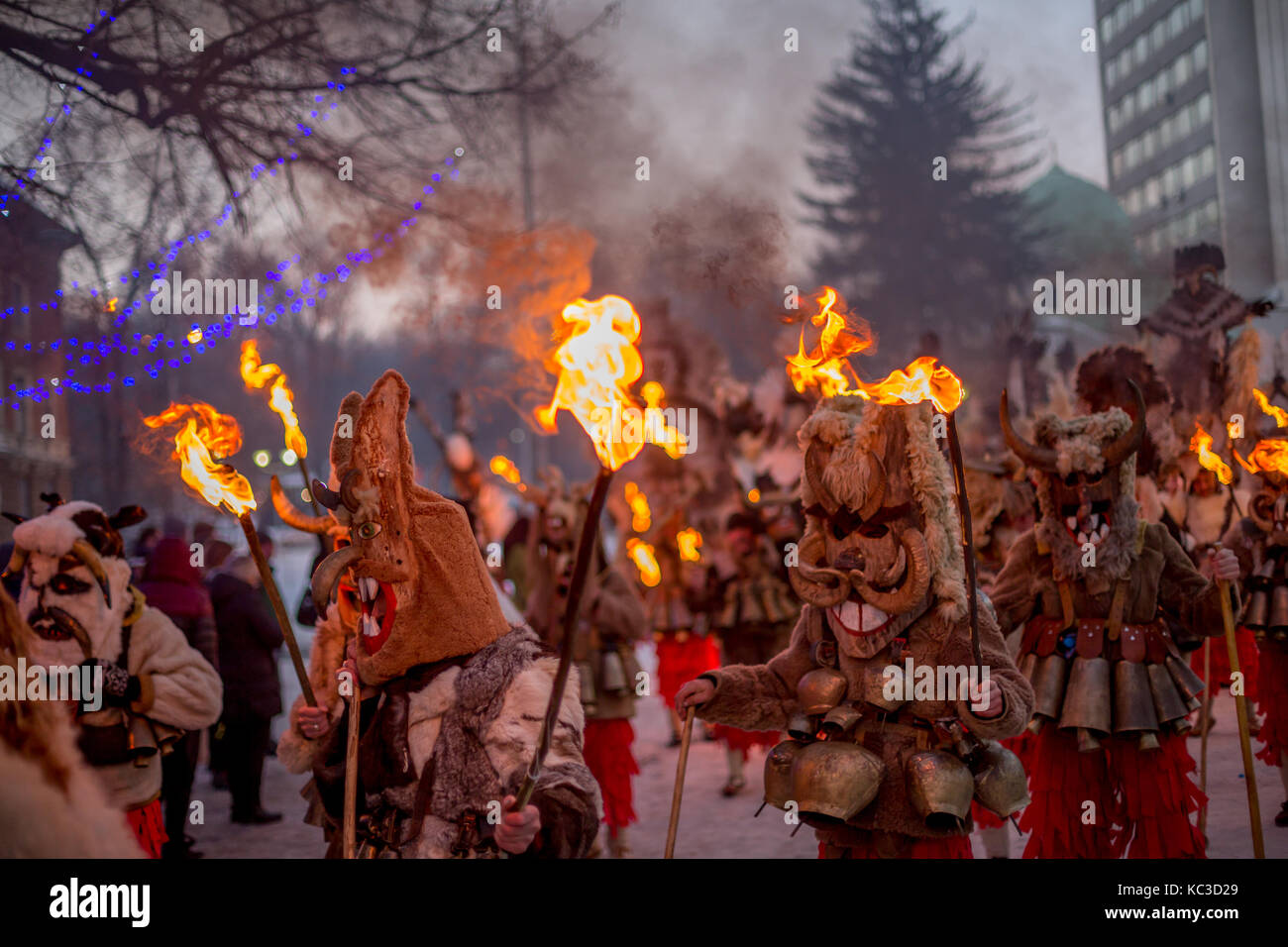 PERNIK, BULGARIA - JANUARY 27, 2017: Masked participants in scary fur costumes and wooden masks with horns are holding burning torches while marching  Stock Photo