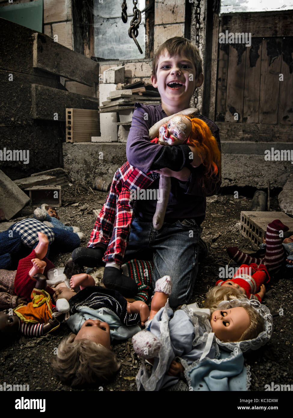 Photo of a creepy young boy holding an old clown doll in an old barn covered in spiderwebs and dust. Stock Photo