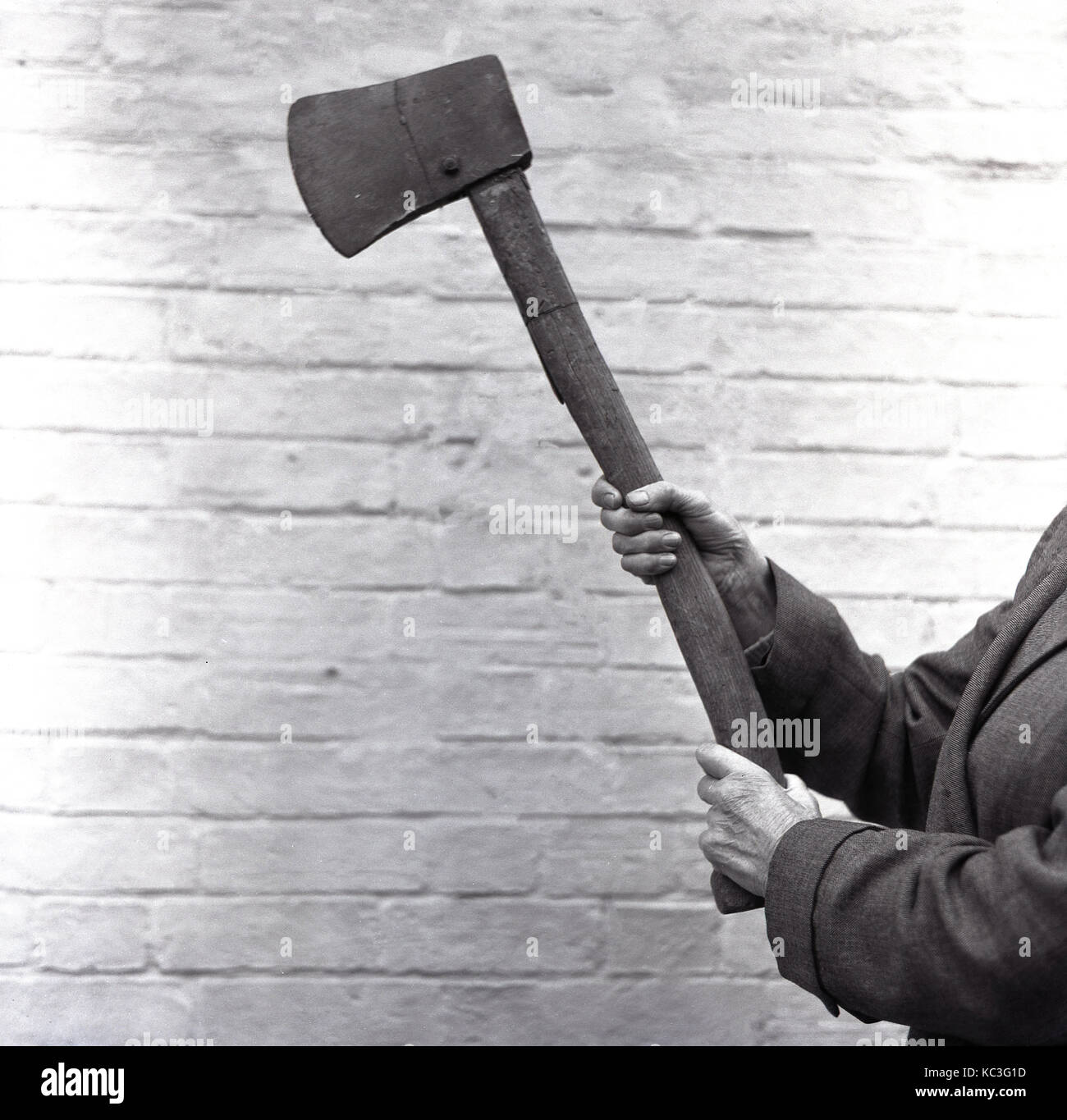 1964, historical, person holding up a large axe, a tool used for splitting wood. The axe has a curved wooden handle and iron blade and is being held to show it, to demonstrate it to an audience, England, UK. Stock Photo