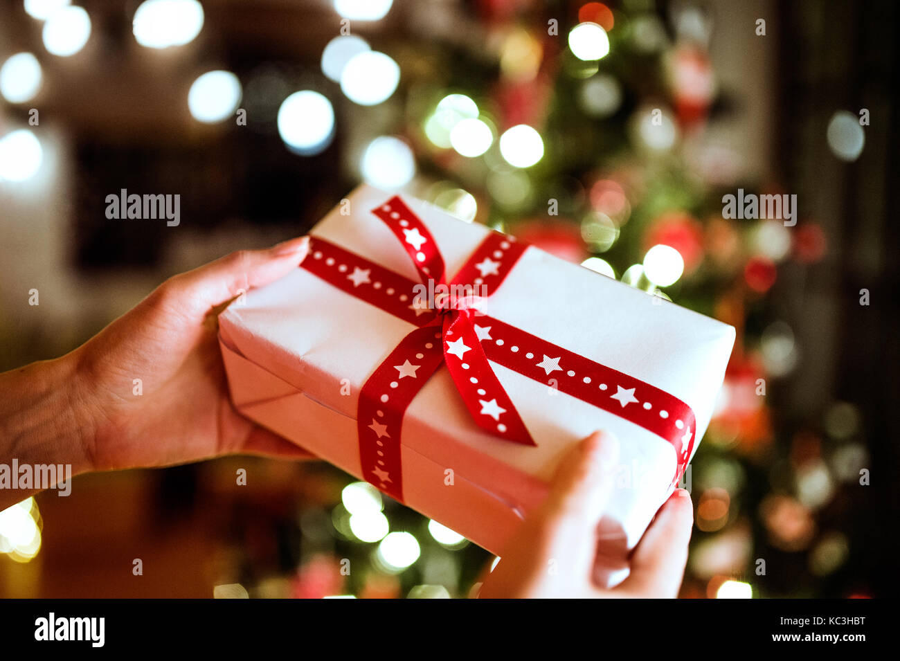 Unrecognizable woman in front of Christmas tree holding present Stock ...
