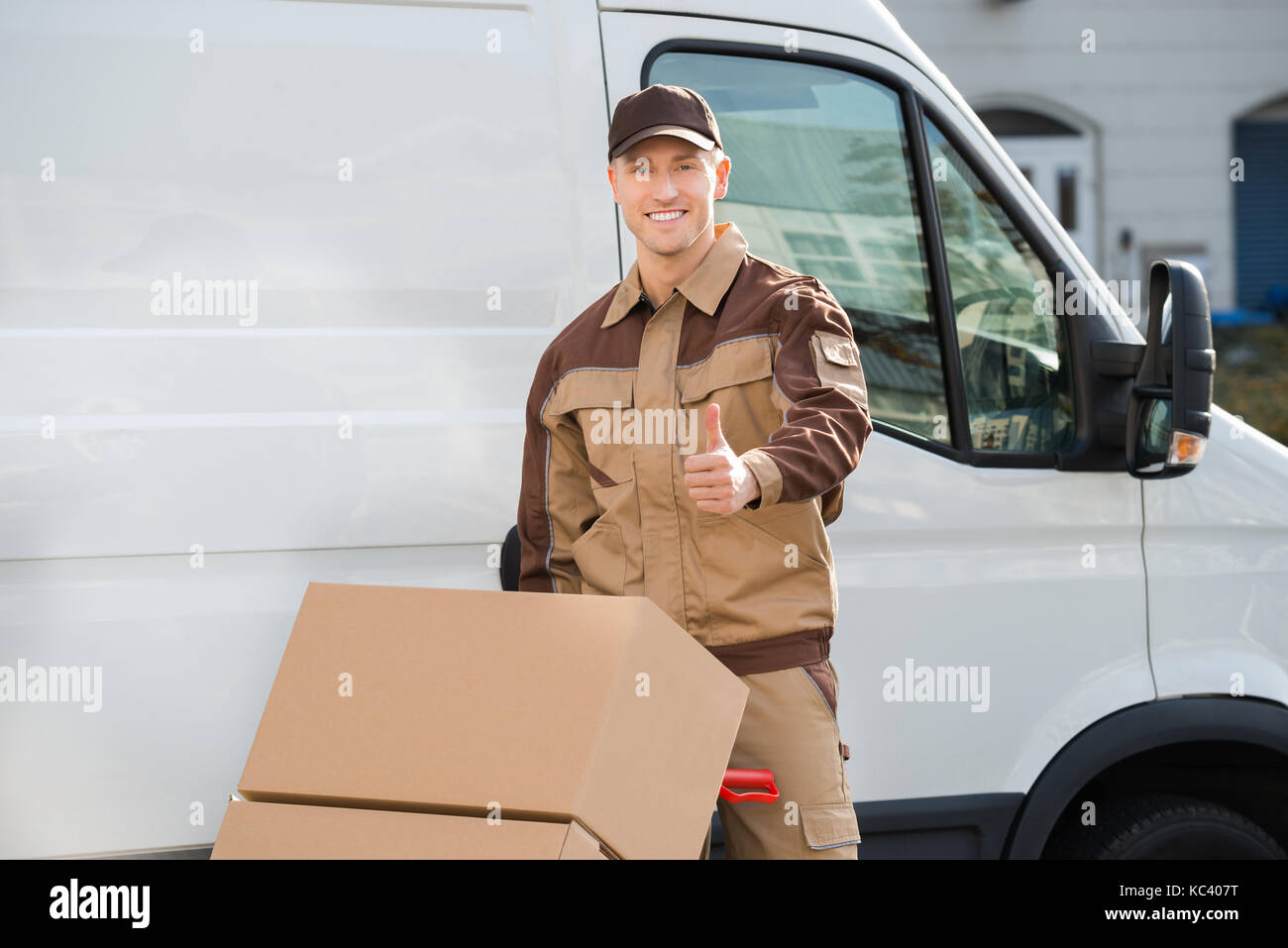 Portrait of confident delivery man pushing parcels on handtruck against van Stock Photo