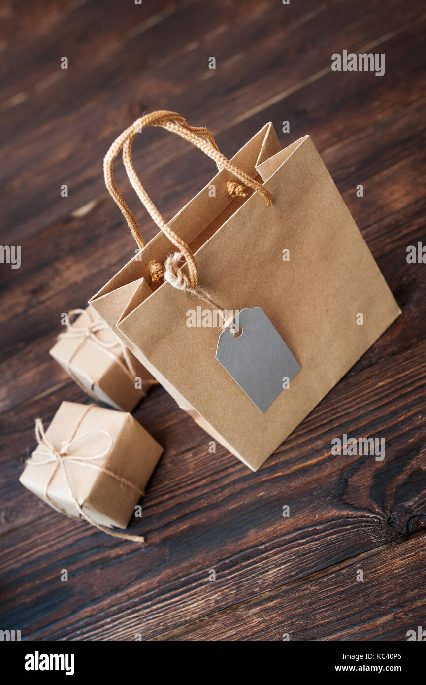 Mockup Paper bag from kraft paper with gift tag and Christmas gift boxes on a wooden background Stock Photo