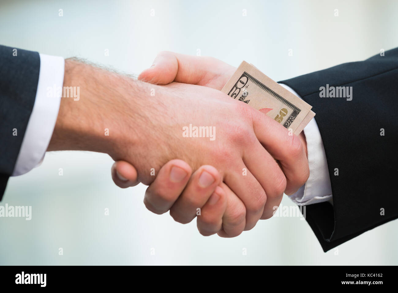 Cropped image of businessman bribing partner while shaking hand outdoors Stock Photo