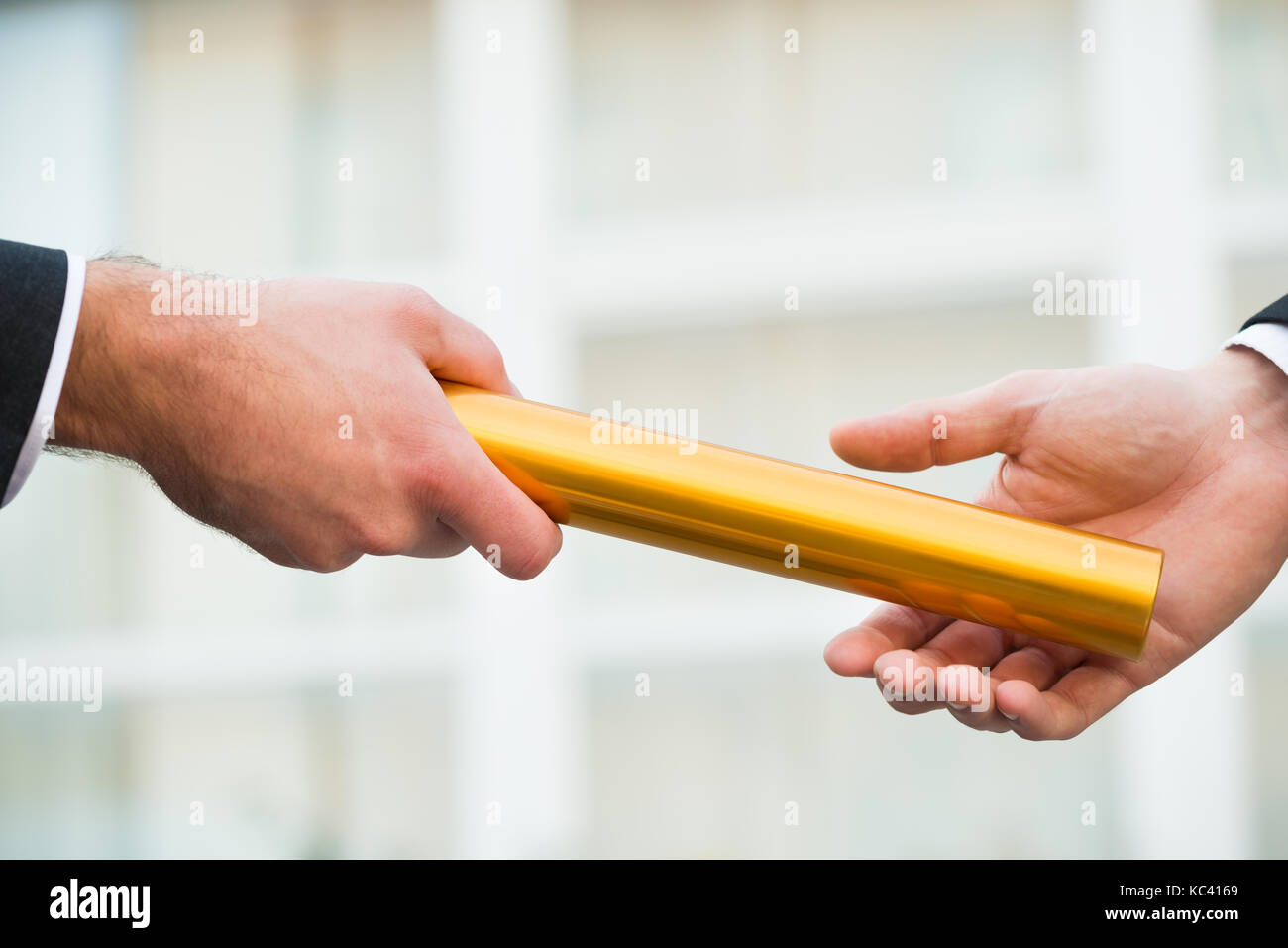 Cropped hand of businessman giving golden relay baton to colleague outdoors Stock Photo