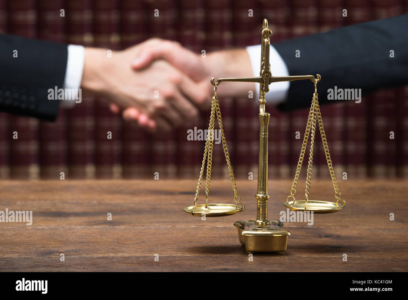 Justice scale on wooden table with judge and client shaking hands in background at courtroom Stock Photo