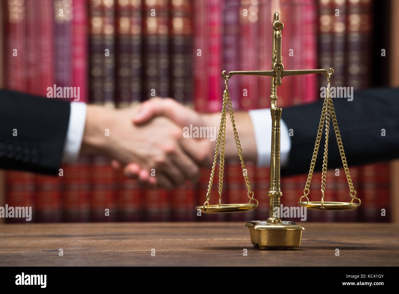 Justice scale on wooden table with judge and client shaking hands in background at courtroom Stock Photo