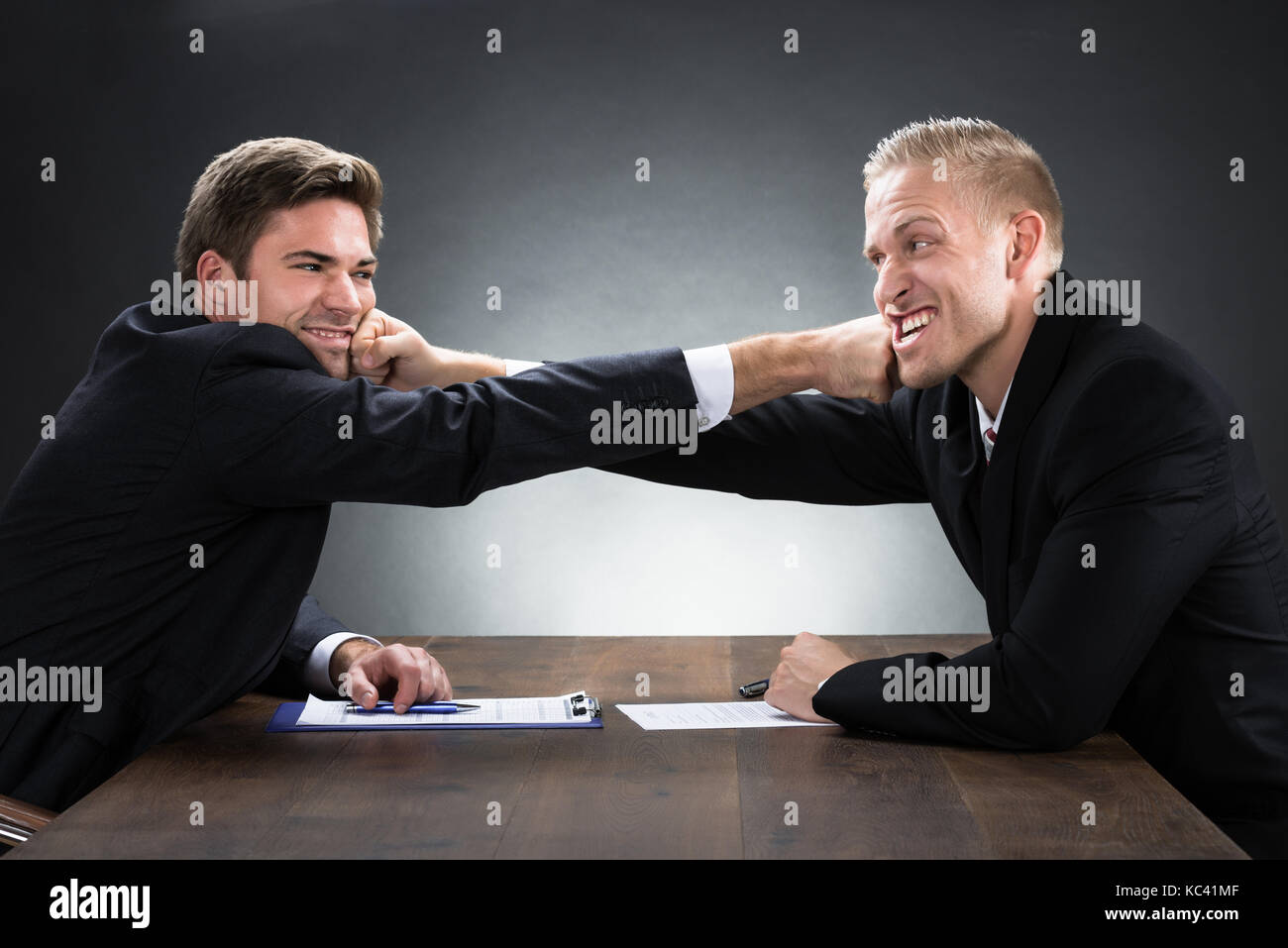 Young businessmen fighting at wooden desk against gray background Stock Photo