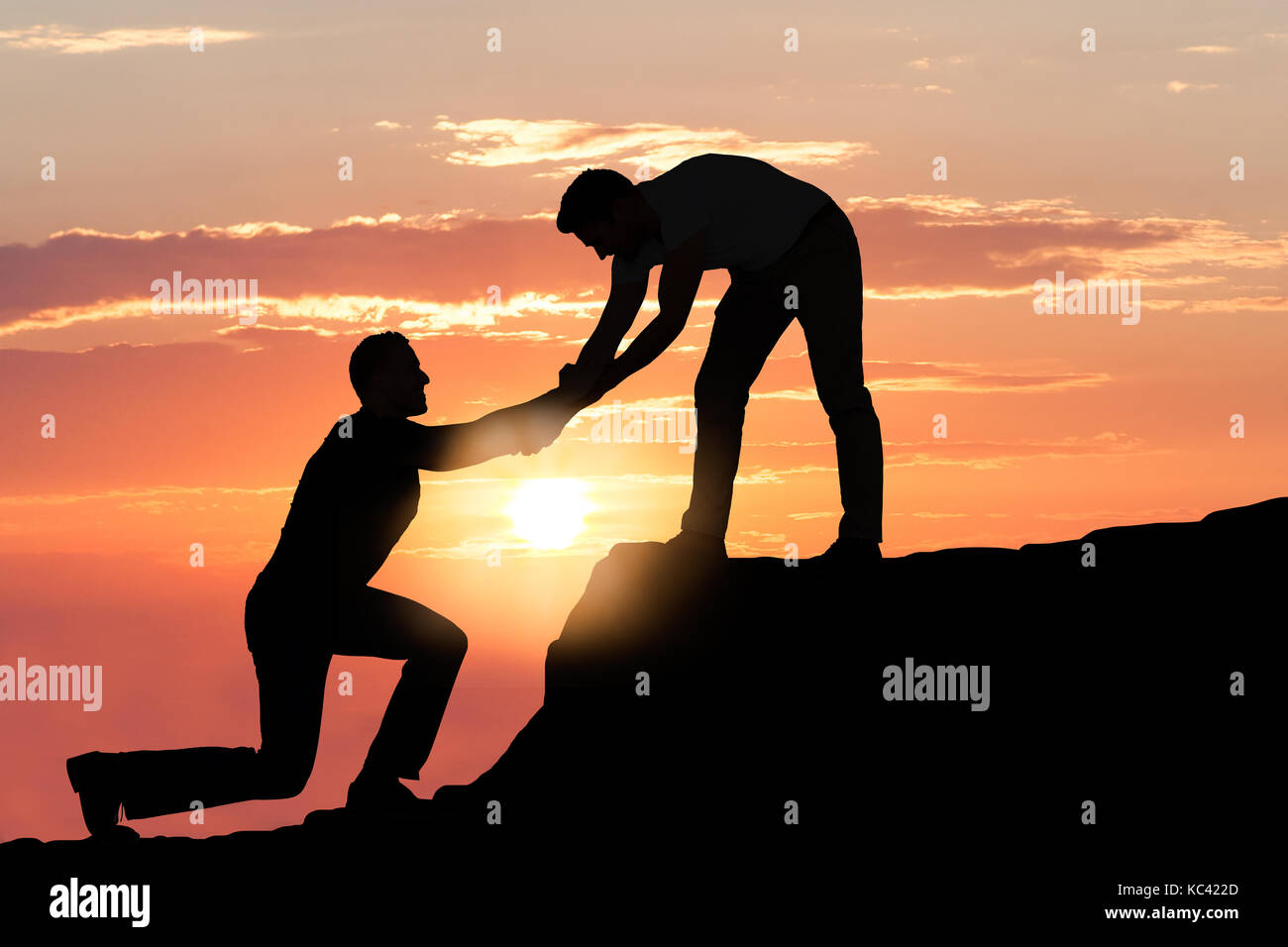 Silhouette young man assisting male friend in climbing rock during sunset Stock Photo