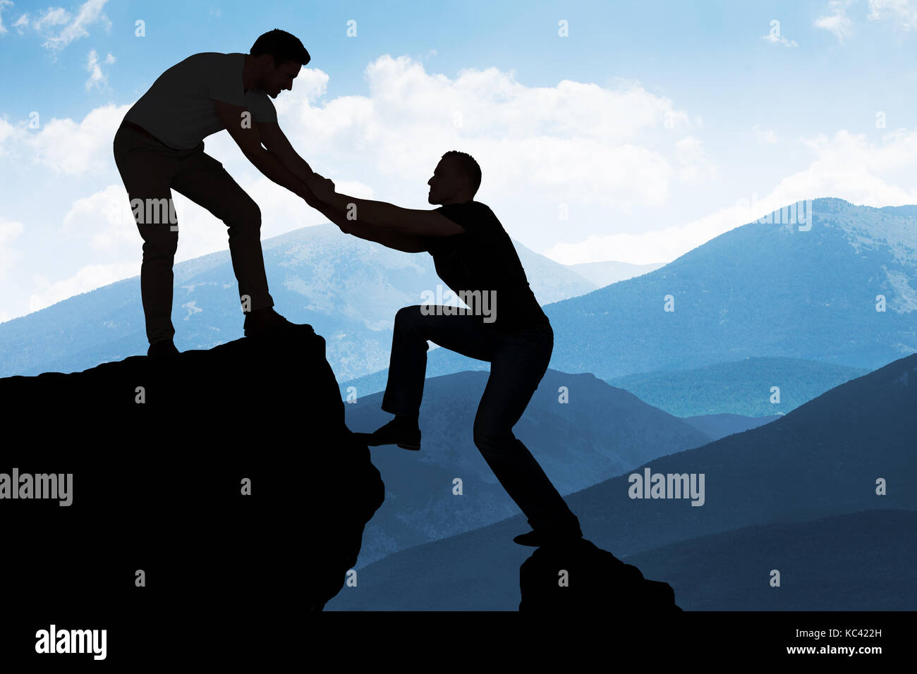 Silhouette young man assisting male friend in climbing rock Stock Photo