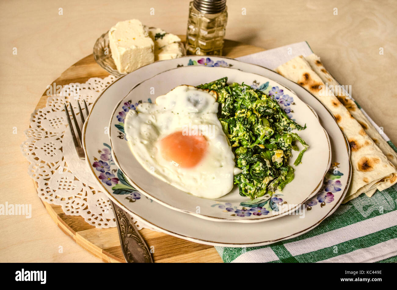 Spinach with fried eggs and sheep cheese,pita on striped chopping board
