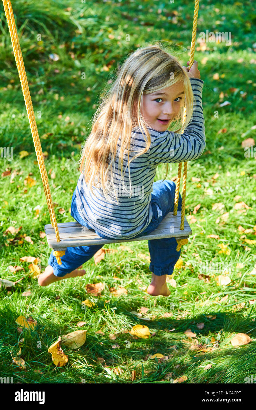 Little child blond girl having fun on a swing outdoor. Summer playground. Girl swinging high. Young child on swing in garden Stock Photo