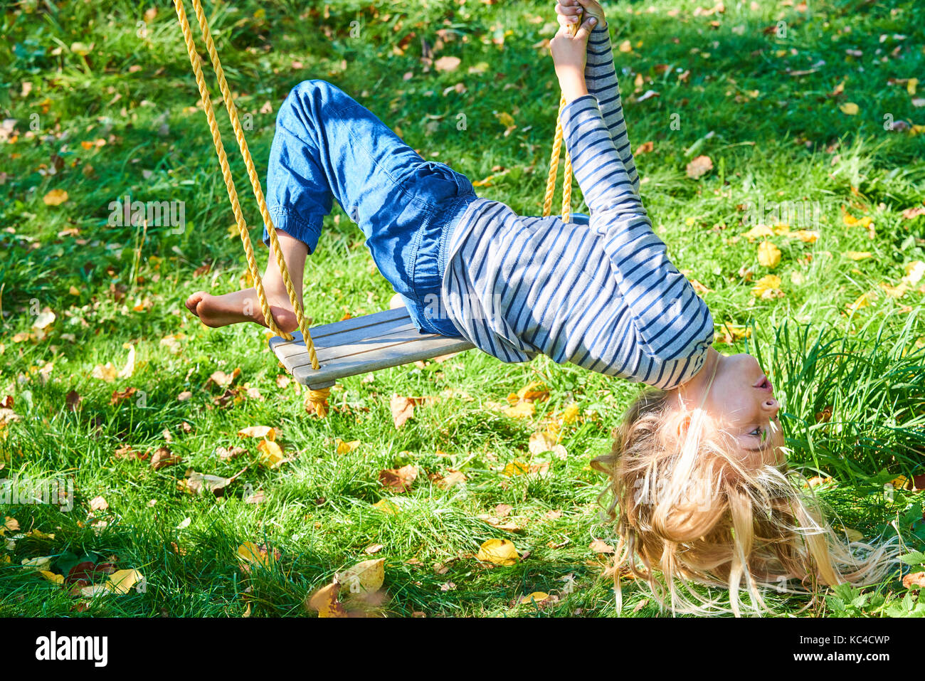 Little child blond girl having fun on a swing outdoor. Summer playground. Girl swinging high. Young child on swing in garden Stock Photo