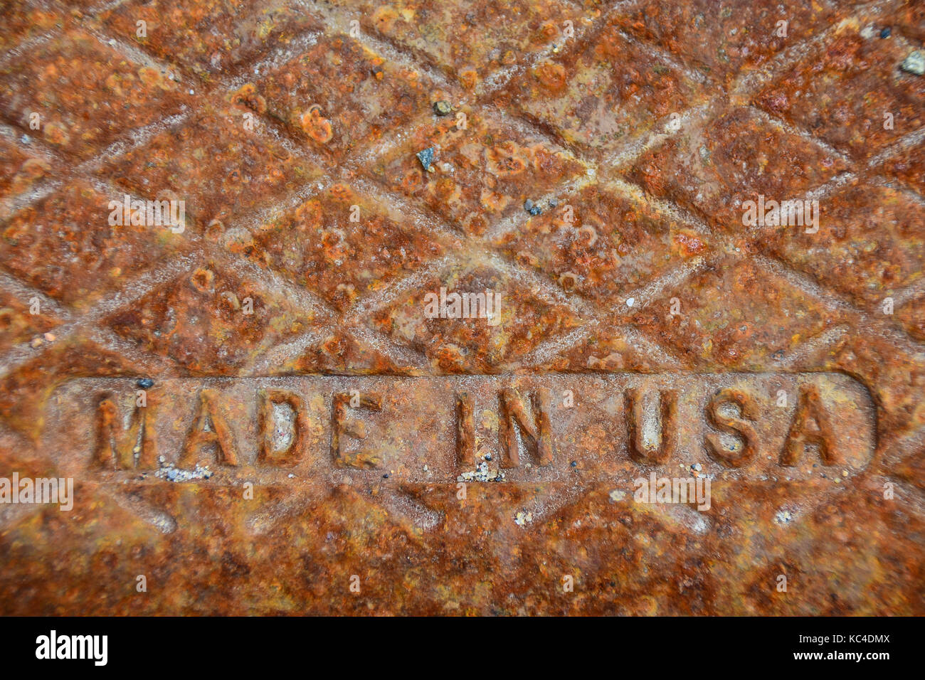 Rusted old Made in USA cast iron cover over storm sewer drain - concept against importing vs. manufacturing in USA and job losses. Stock Photo